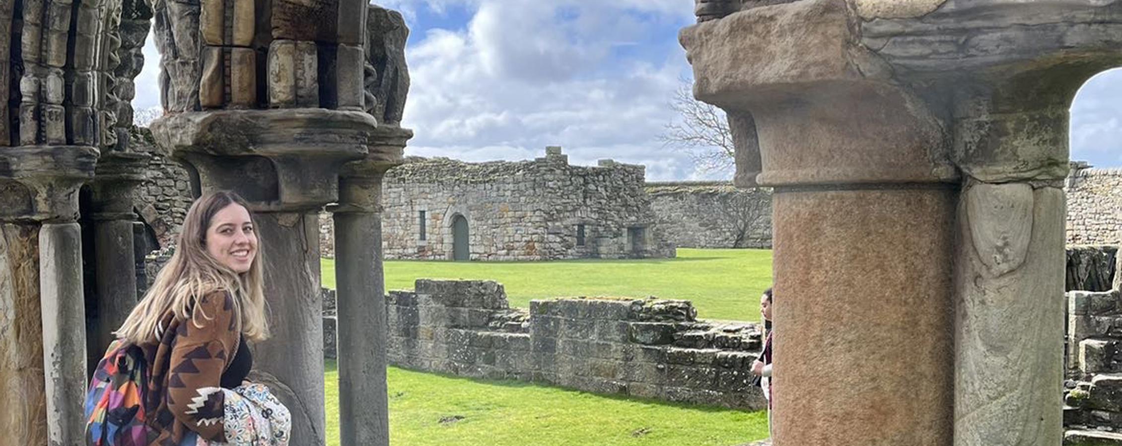 A student stands among the remains of stone architecture in Scotland.