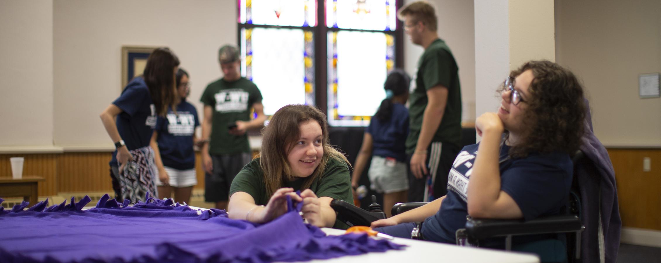 Two students help make blankets at a church.