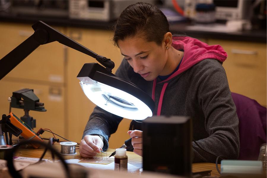 A student solders groups of micro wires under a large light.