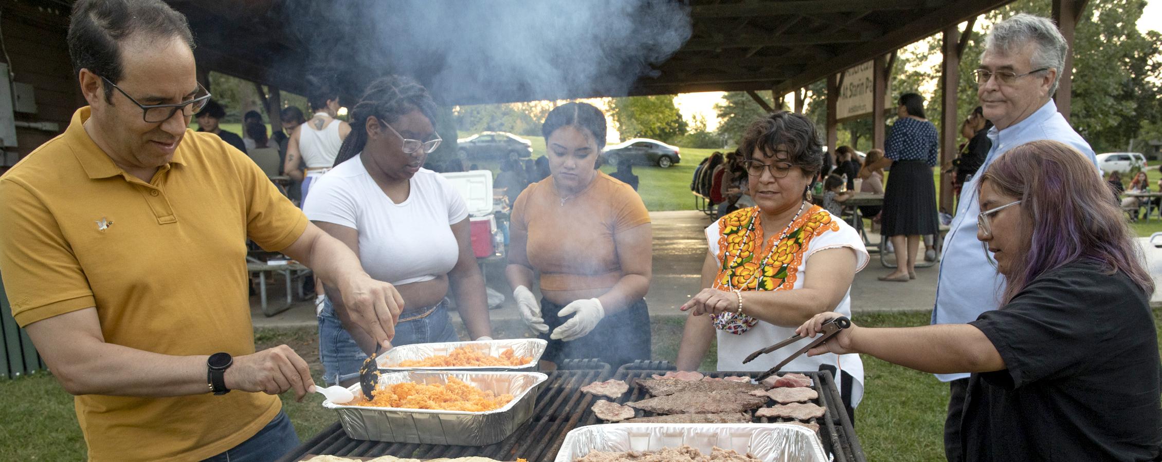 People gather around outdoor grills making food.