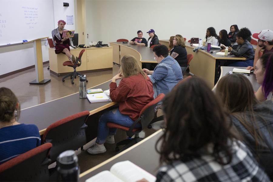 A person with pink hair reads at the front of class.