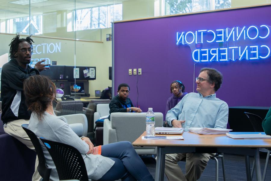 People sit at tables with a purple wall in the background and neon letters that say Connection Centered.