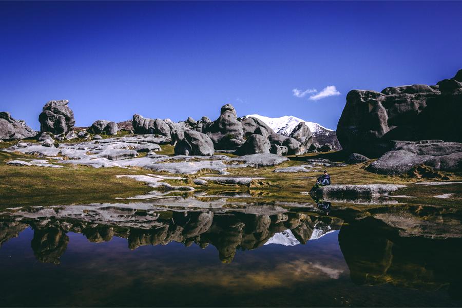 A person sits next to a pool of water amidst trees and mountains.