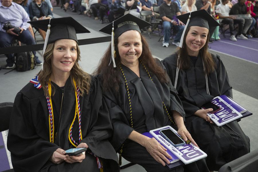 Three adult graduates sit together at commencement.