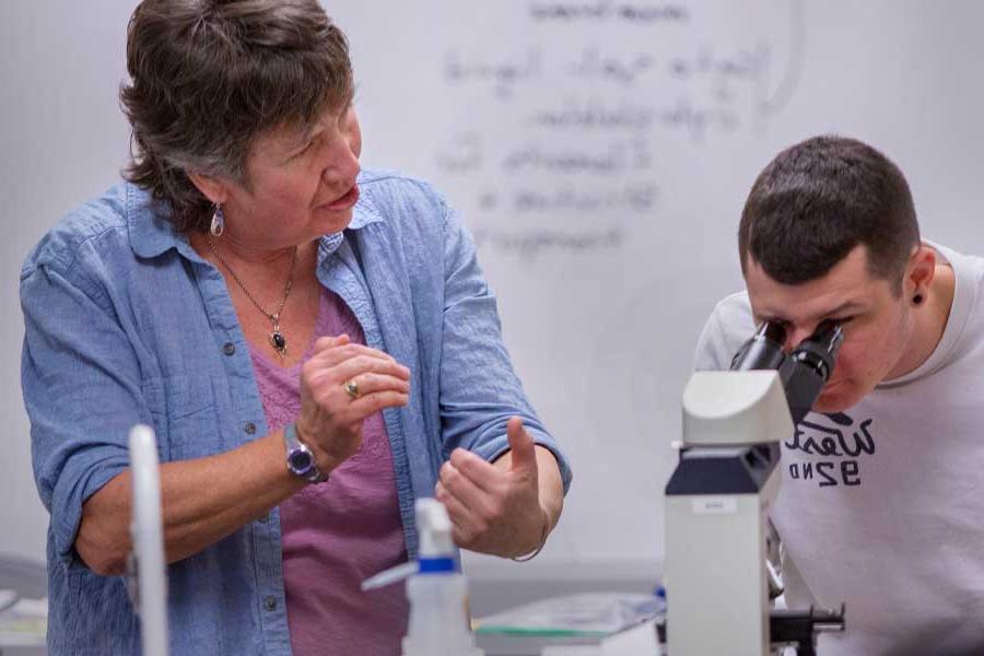 A professor and student examining a microscope