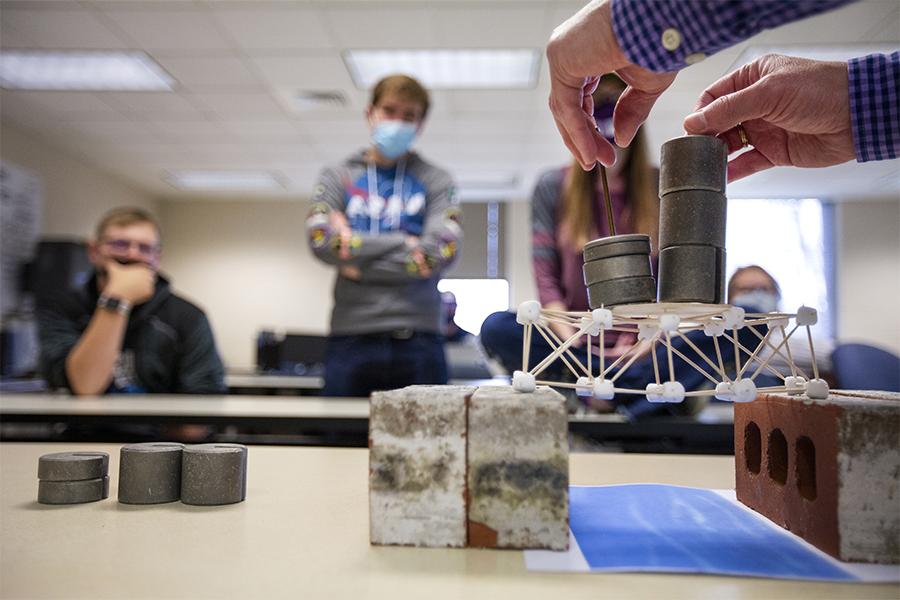 An engineering class creates tests bridges with marshmallows, toothpicks and weights.