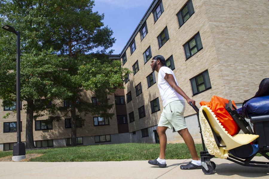 A student pulls a cart full of their belongings in front of a brick building.